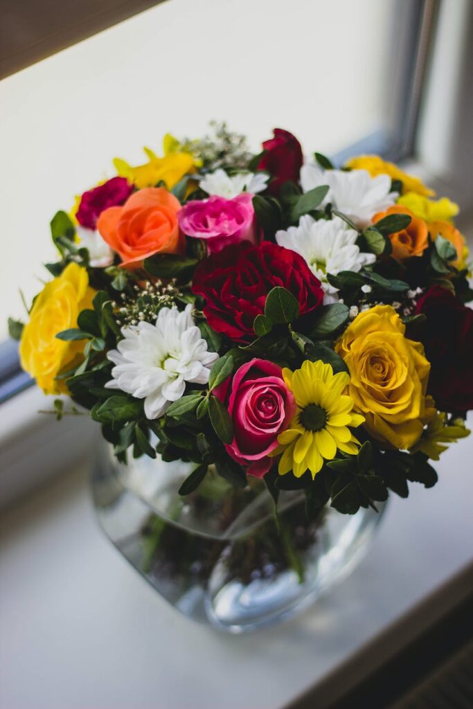 mums and rose flower in clear glass vase centerpiece beside glass window