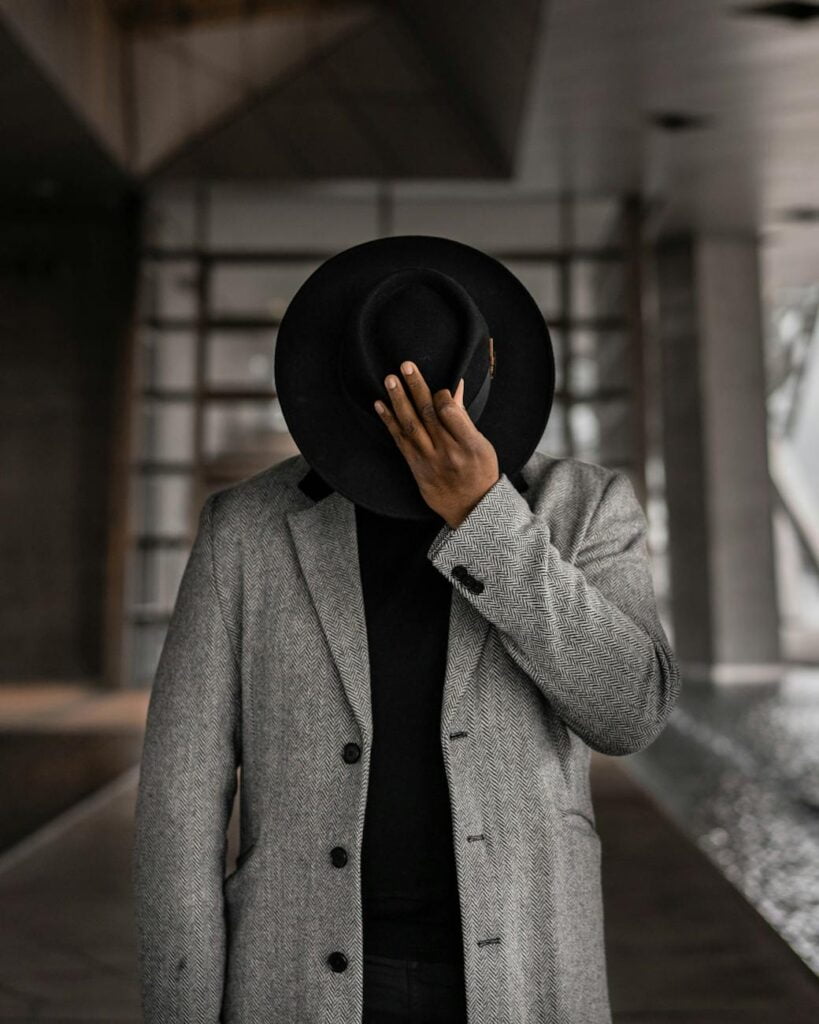 person in gray coat holding black hat